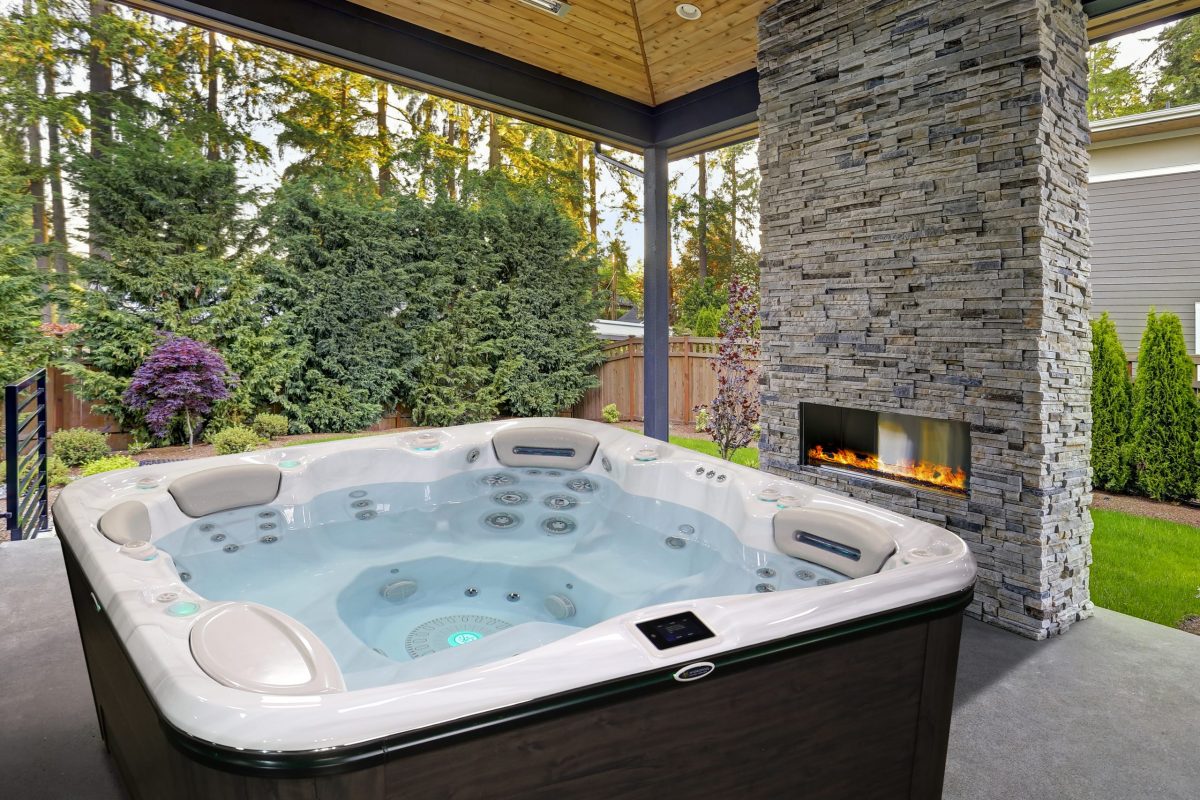 New modern home features a backyard with patio New modern home features a backyard with covered patio accented with stone fireplace, vaulted ceiling with skylights and furnished with gray wicker sofa placed on concrete floor. Northwest, USA
